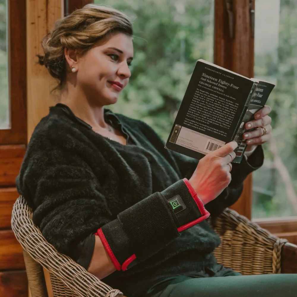 Woman in her 60s wearing WREN wrap on knee while reading in a cozy armchair, relaxed and comfortable
